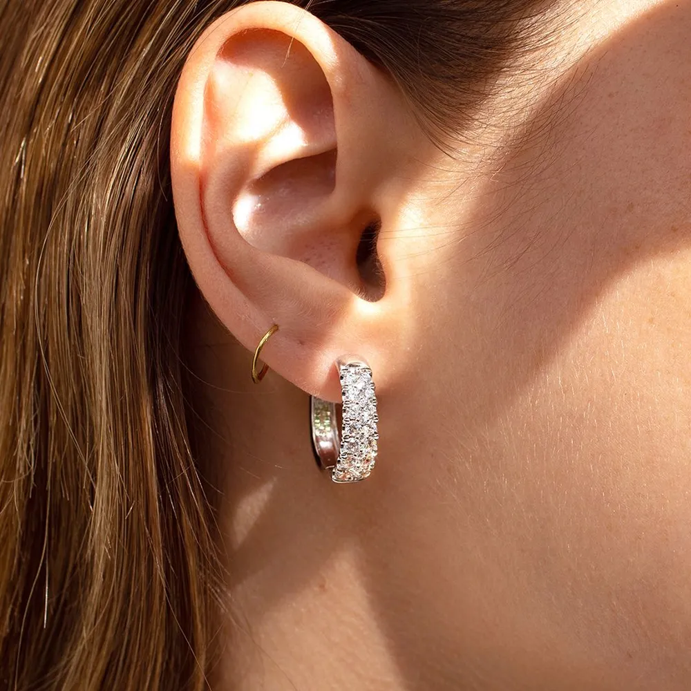 Close-up of a woman's ear showcasing a sparkling diamond hoop earring and a small gold hoop.