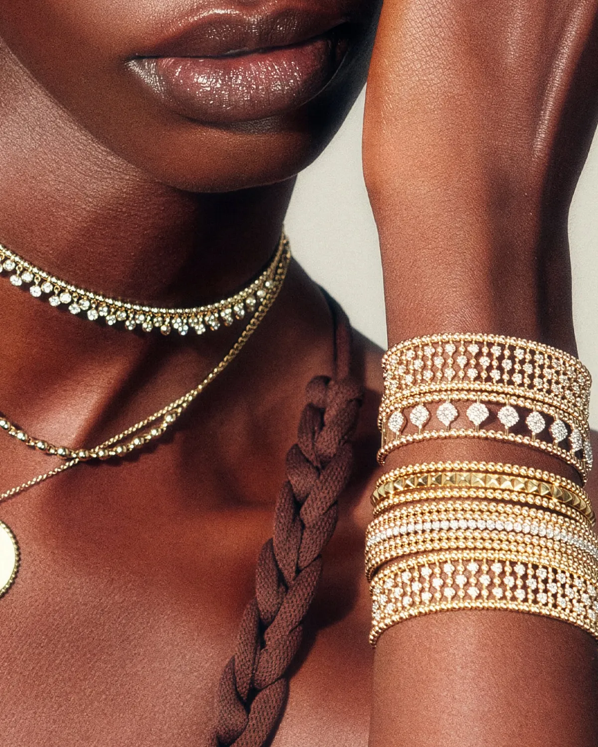 Close-up of a model's neck and wrist adorned with elegant gold and diamond jewelry.
