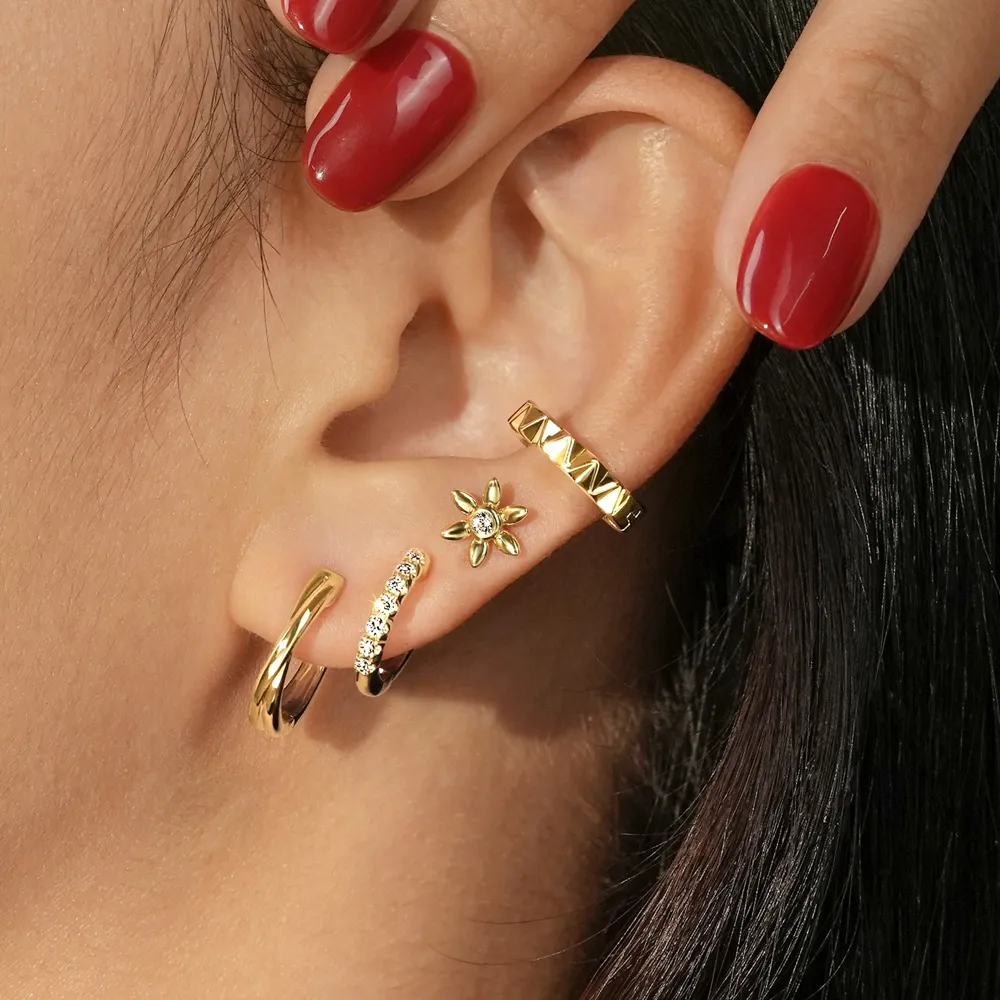 Gold earrings displayed on a model's ear, featuring a floral design and sparkling accents.