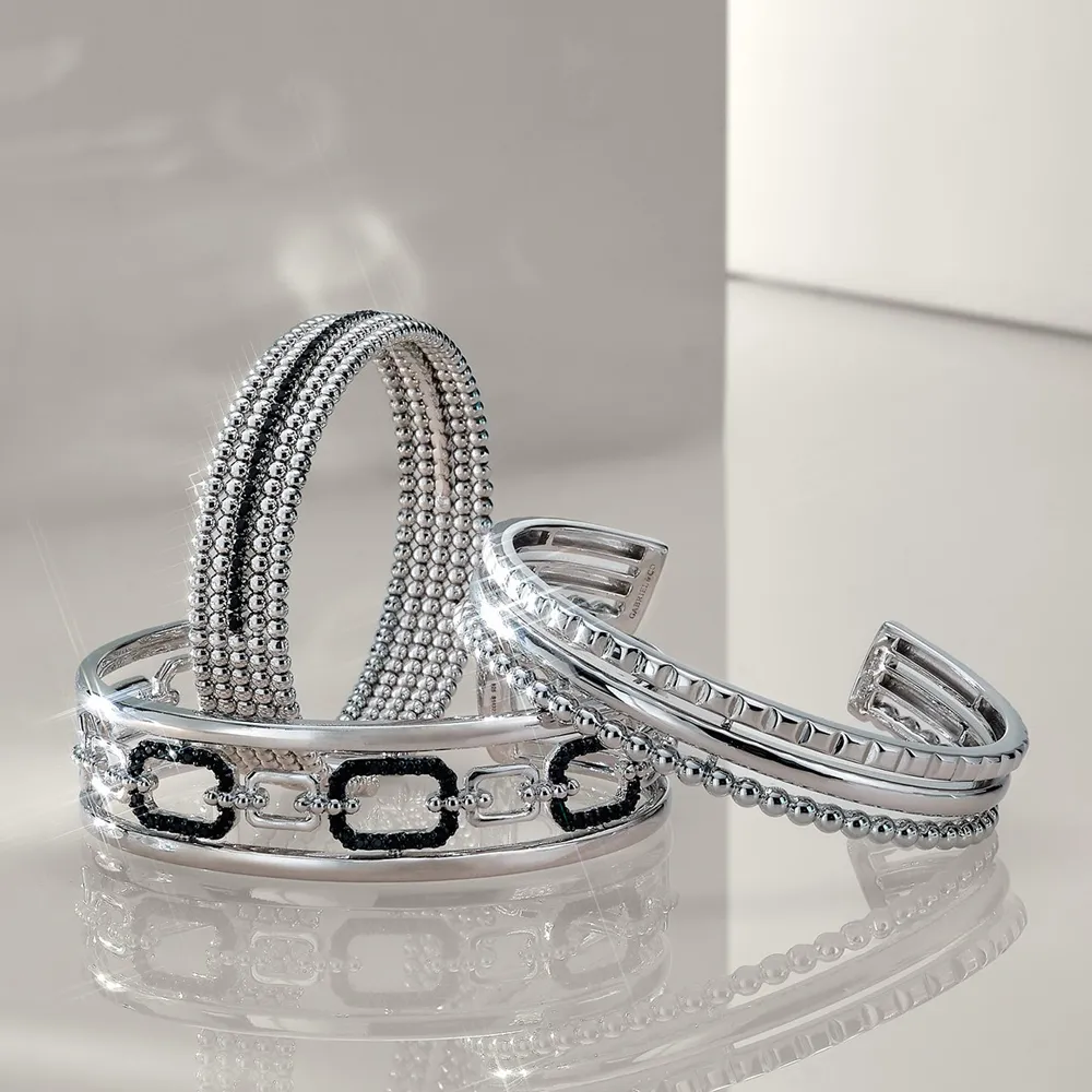 Three elegant silver bracelets with intricate designs displayed on a reflective surface.