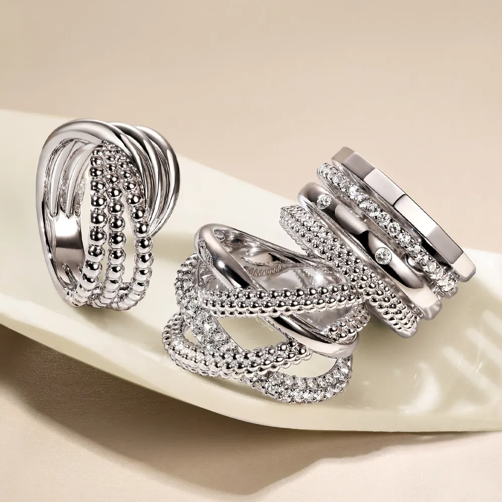 Three elegant silver rings with intricate designs displayed on a cream-colored plate.