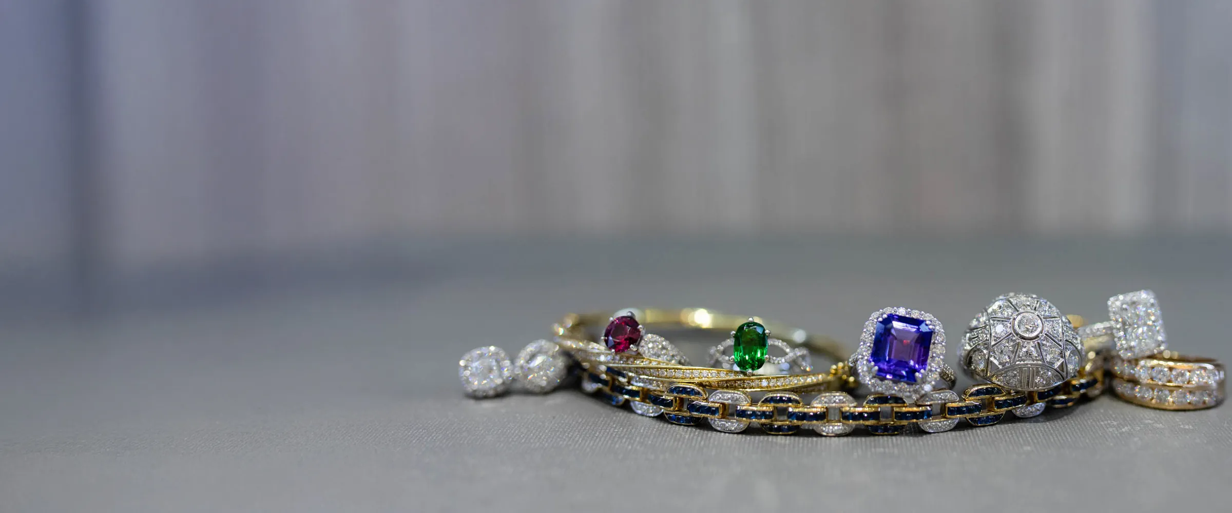 A collection of elegant rings featuring colorful gemstones and diamonds, displayed on a soft surface. 