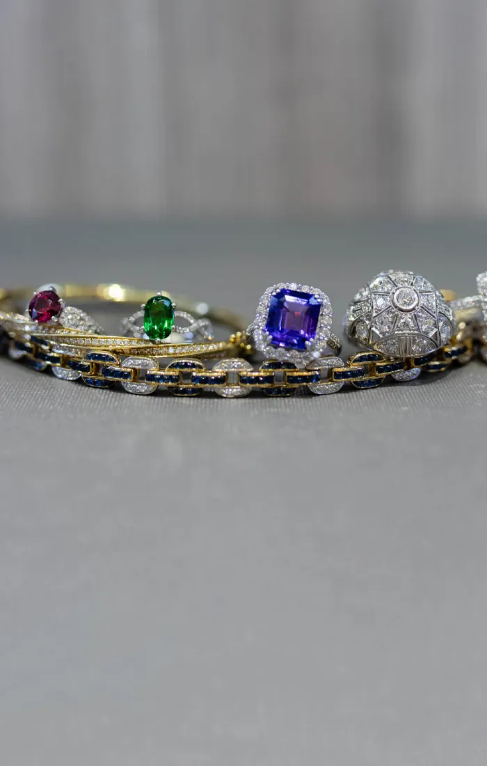 A collection of elegant rings featuring colorful gemstones and diamonds, displayed on a soft surface. 