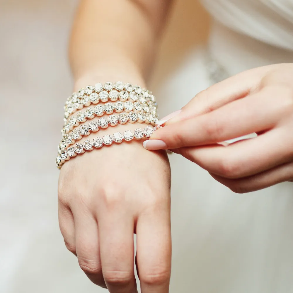 A bride adjusts her sparkling silver bracelets, showcasing elegant jewelry.