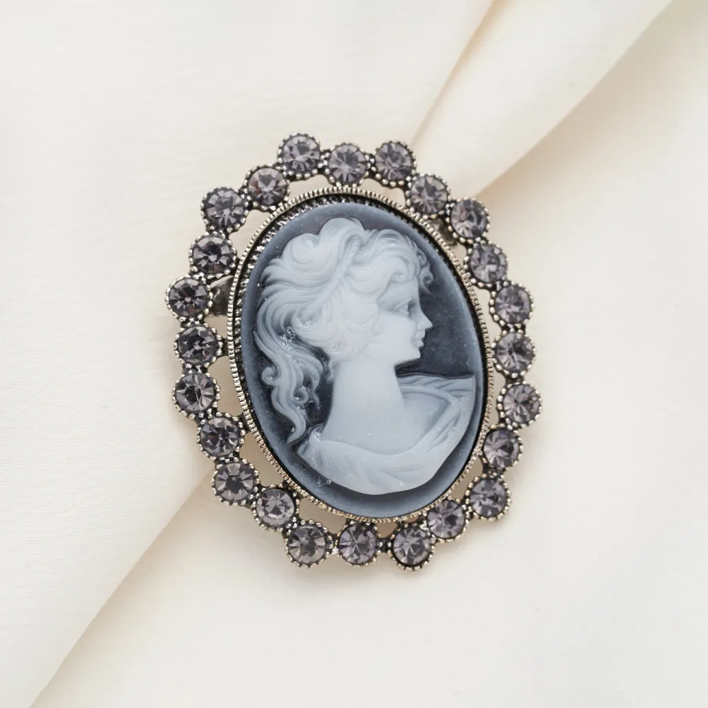 Vintage cameo brooch featuring a woman's profile, surrounded by a decorative border of dark stones.