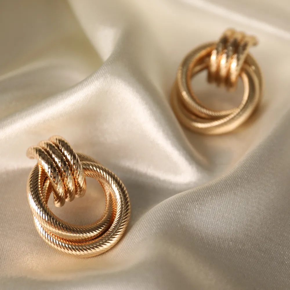 Timeless gold earrings displayed on soft satin fabric, showcasing intricate twisted design.