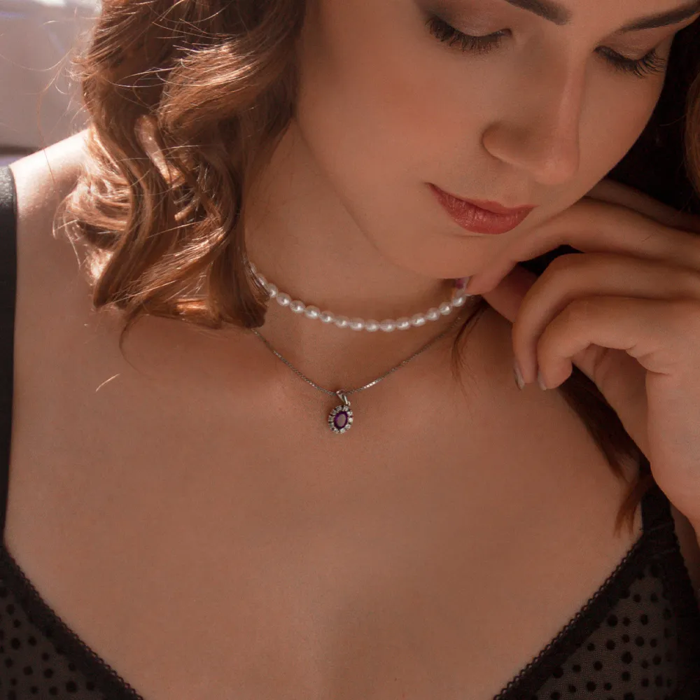 Elegant woman wearing a pearl choker and a silver necklace with a purple pendant, showcasing fine jewelry.