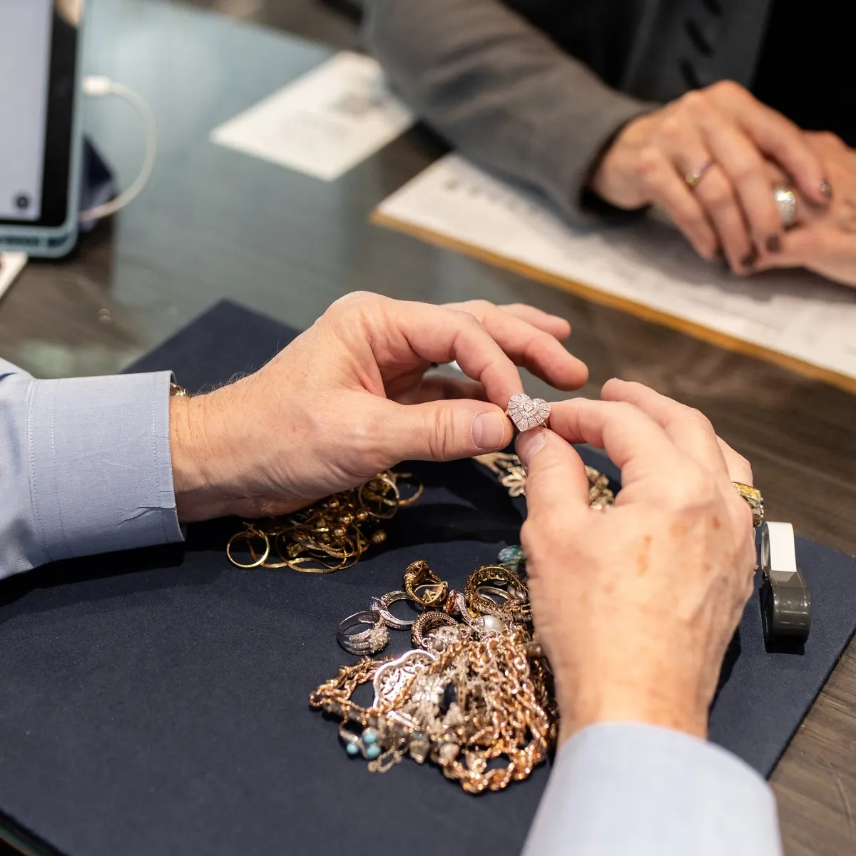 A person examines a heart-shaped ring among various jewelry pieces at Flora Gems, a jewelry store.