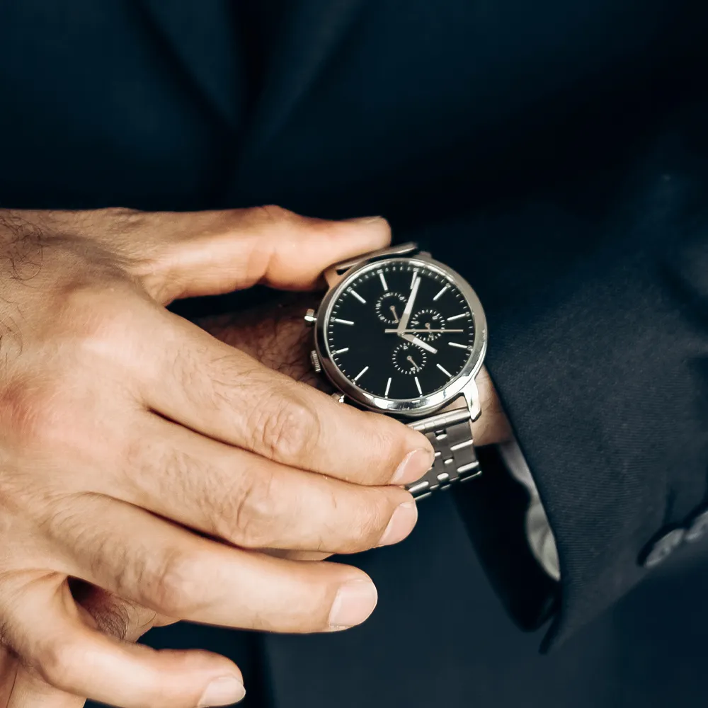 A close-up of a man's hand adjusting a stylish black watch on his wrist, dressed in a suit.