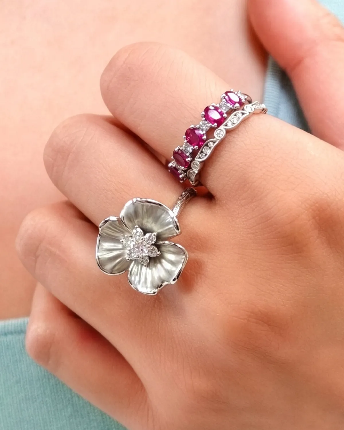 Two elegant rings on a hand: one with a flower design and the other with pink gemstones.