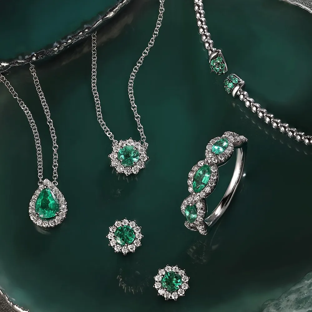 Emerald jewelry set featuring necklaces, earrings, and a ring, displayed on a dark green background.