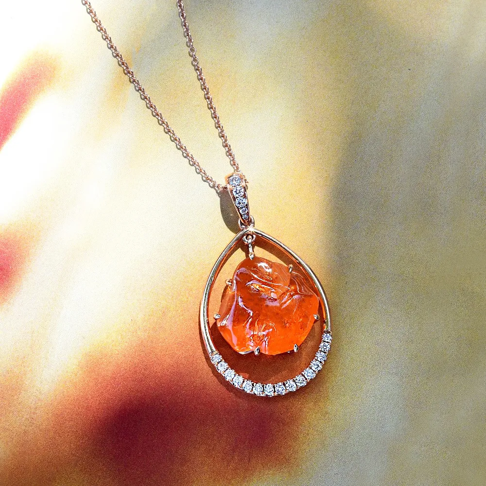 Elegant orange garnet pendant necklace with diamond accents, displayed against a soft background.