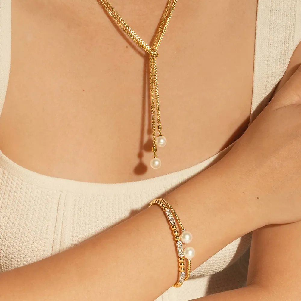 Gold pearl necklace and bracelet set worn on a model's arm, showcasing elegant jewelry from Flora Gems.
