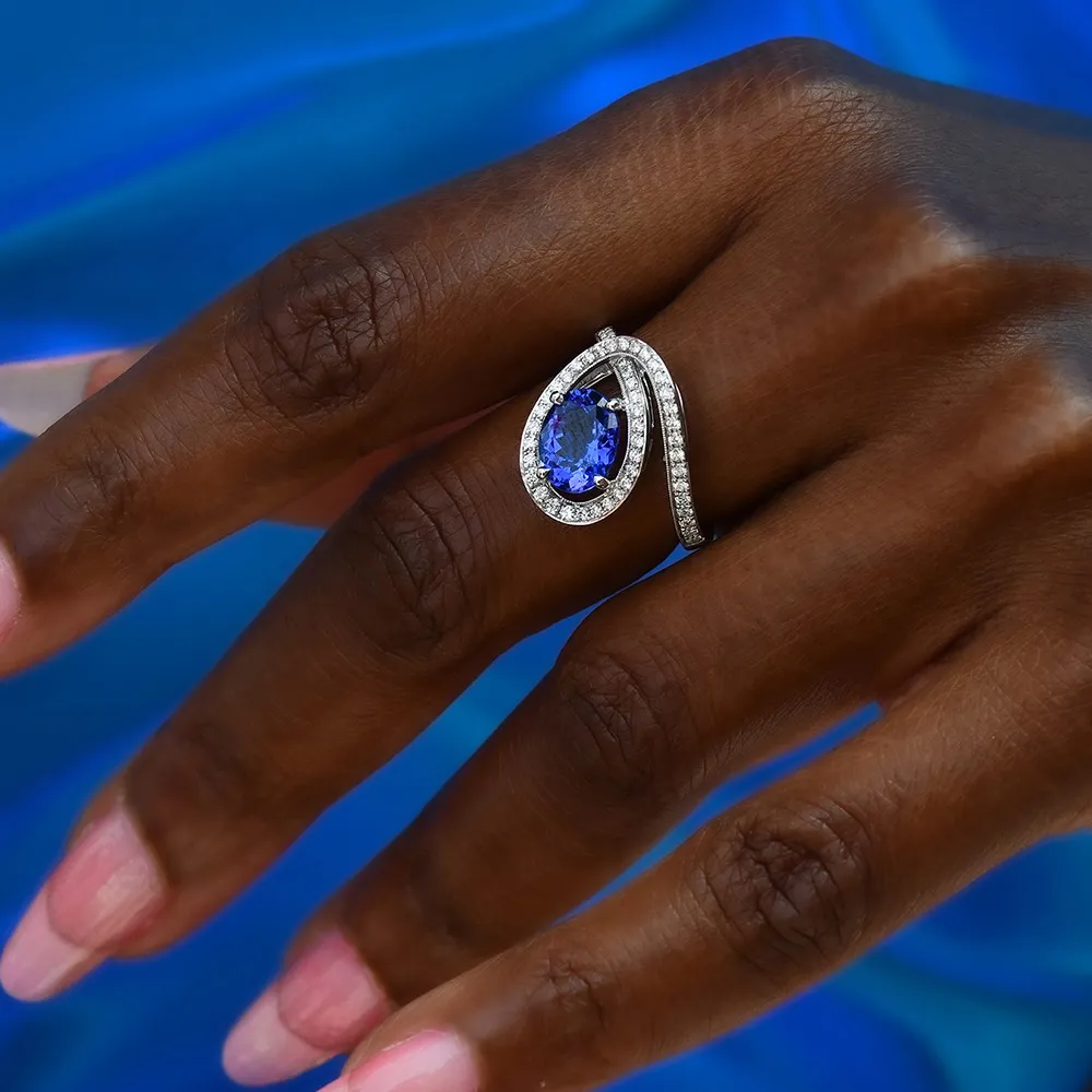 Elegant tanzanite ring with diamonds on a hand against a blue background.
