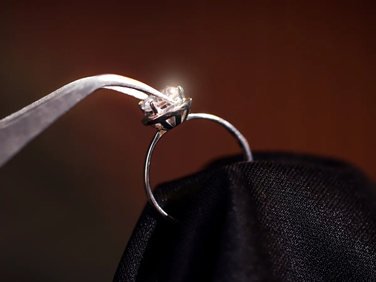 Close-up of a silver ring being held with tweezers, showcasing its intricate design. Visit Flora Gems for jewelry repair.