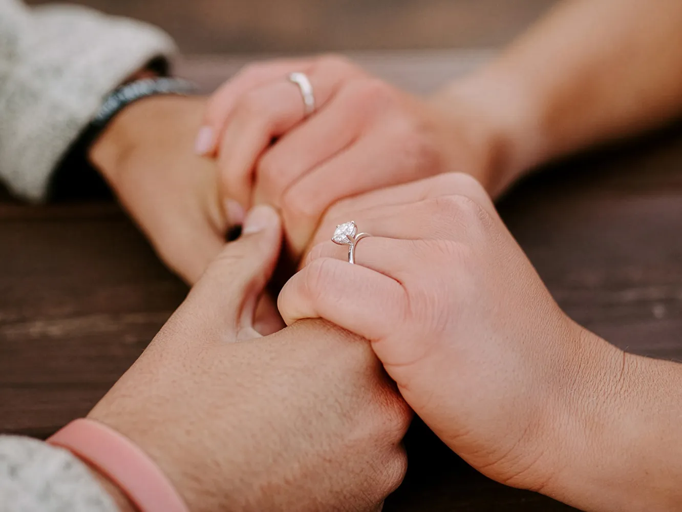 Two hands holding each other, showcasing engagement rings, symbolizing love and commitment. Click to explore Flora Gems jewelry.