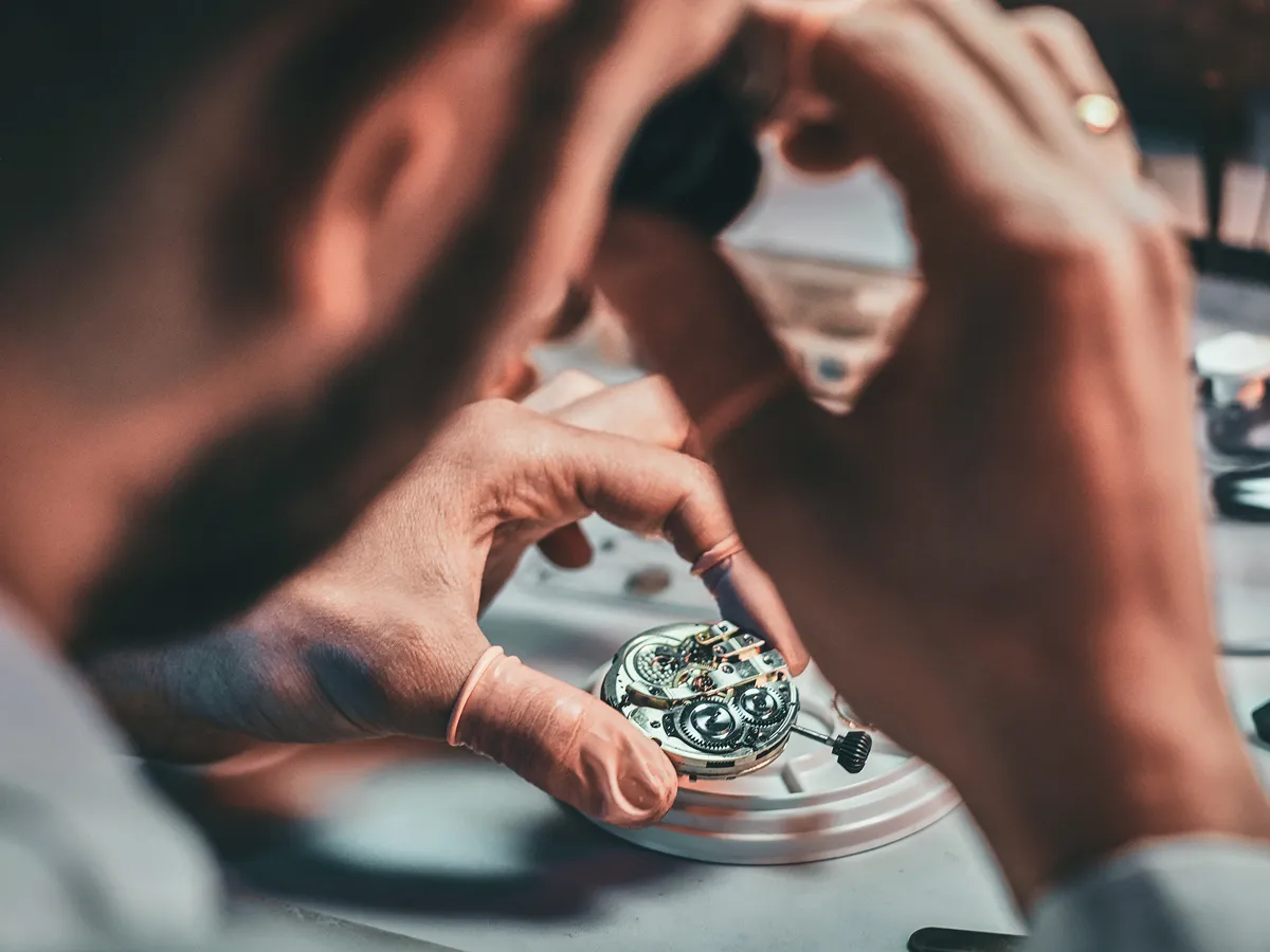 A watchmaker carefully assembles a watch movement, showcasing intricate gears and craftsmanship.