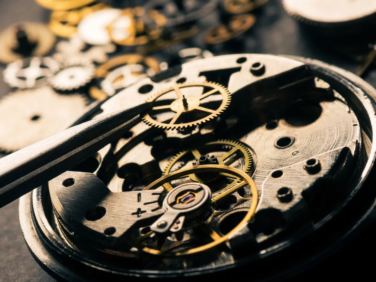 Close-up of watch gears being repaired with tweezers, showcasing intricate mechanics. Visit Flora Gems for watch repairs.