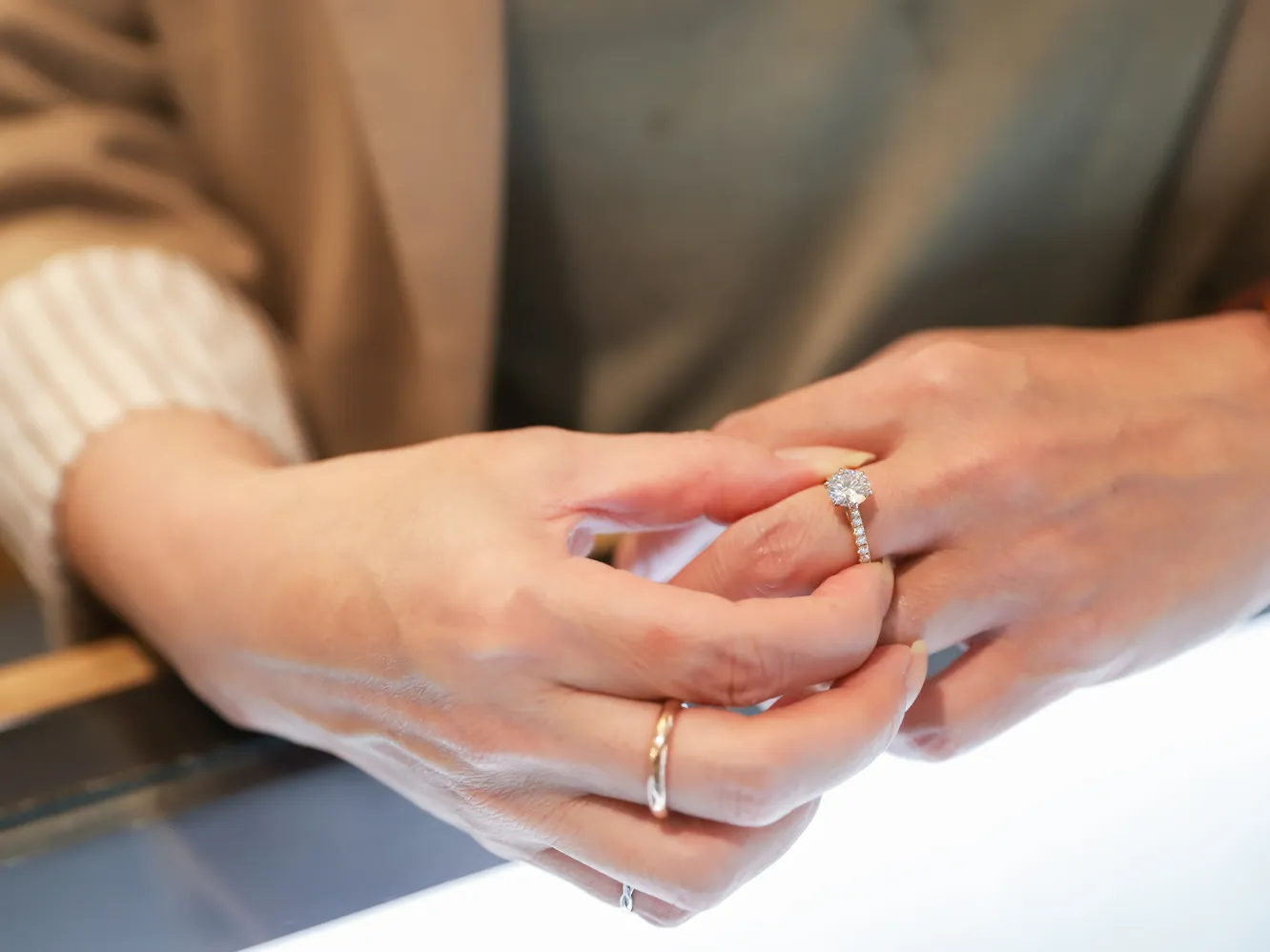 A person trying on a diamond engagement ring at a jewelry store. Visit Flora Gems for more.