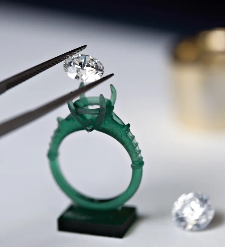 A diamond being placed into a green ring setting with tweezers.