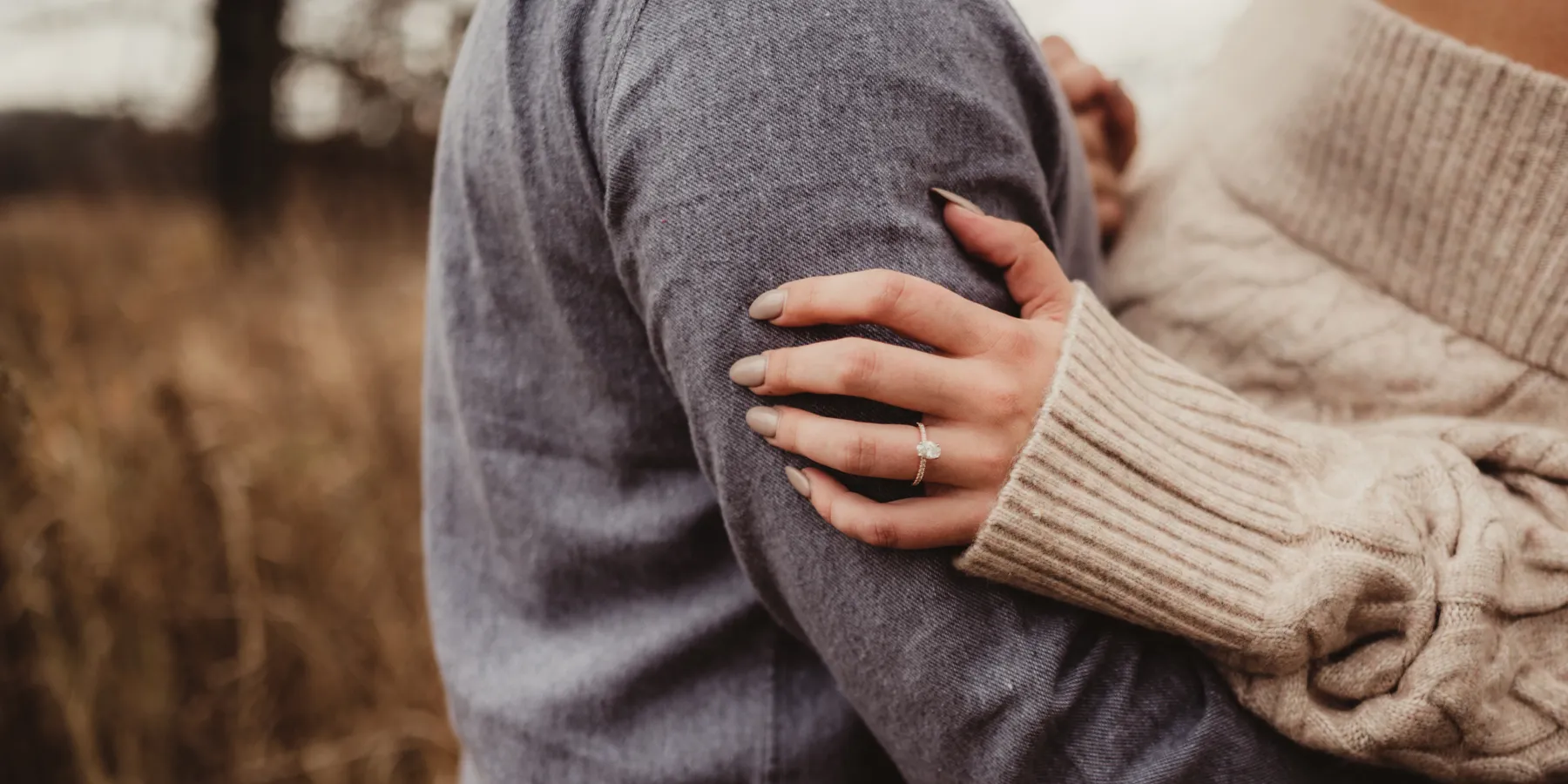 A couple embraces, showcasing an engagement ring on the woman's hand.