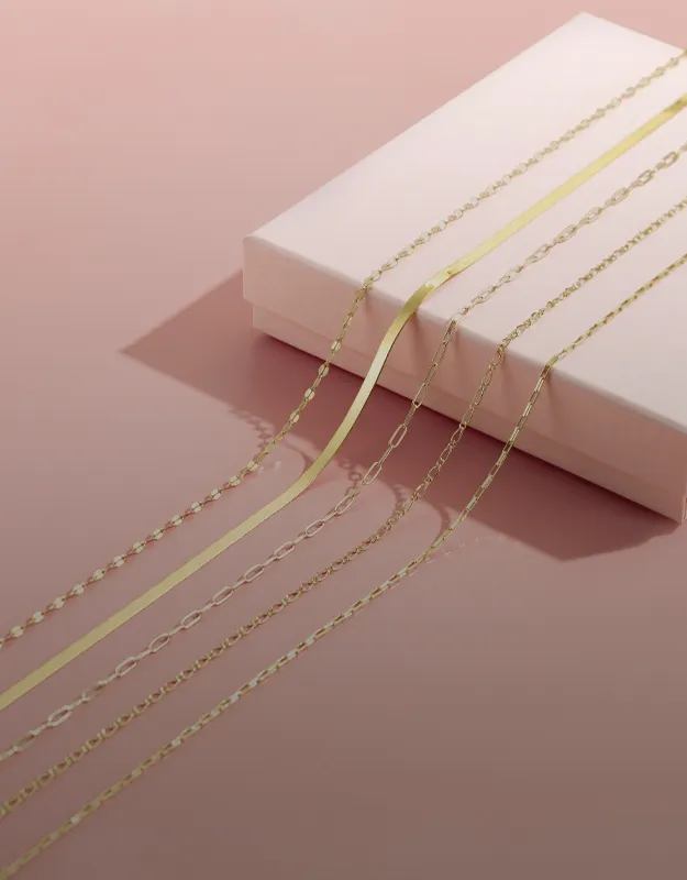 Layered gold chains displayed on a pink background, inviting viewers to explore chains at Futer Bros Jewelers.