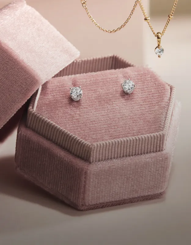 Elegant diamond earrings in a pink velvet box, with a gold necklace above. Click to explore more earrings at Futer Bros Jewelers