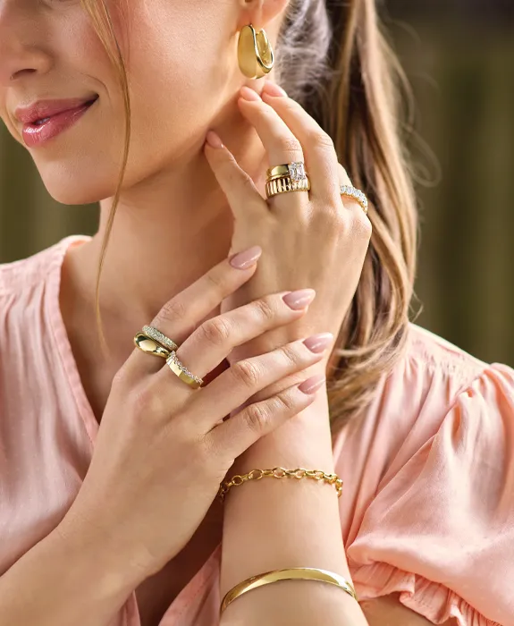 Woman wearing gold jewelry including rings, earrings, and bracelets. Click to shop fashion jewelry at Futer Bros Jewelers.