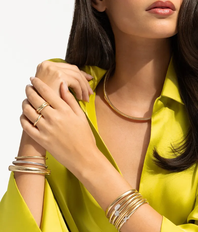Elegant woman in yellow blouse wearing gold jewelry. Click to Shop Now at Futer Bros Jewelers.