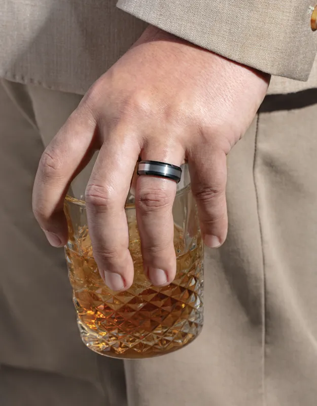Man's hand holding a glass with a black and silver wedding band. Click to explore men's wedding bands at Futer Bros Jewelers.