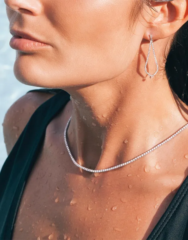 Model wearing elegant diamond earrings and a necklace, with water droplets on her skin. Shop neckwear at Futer Bros Jewelers.