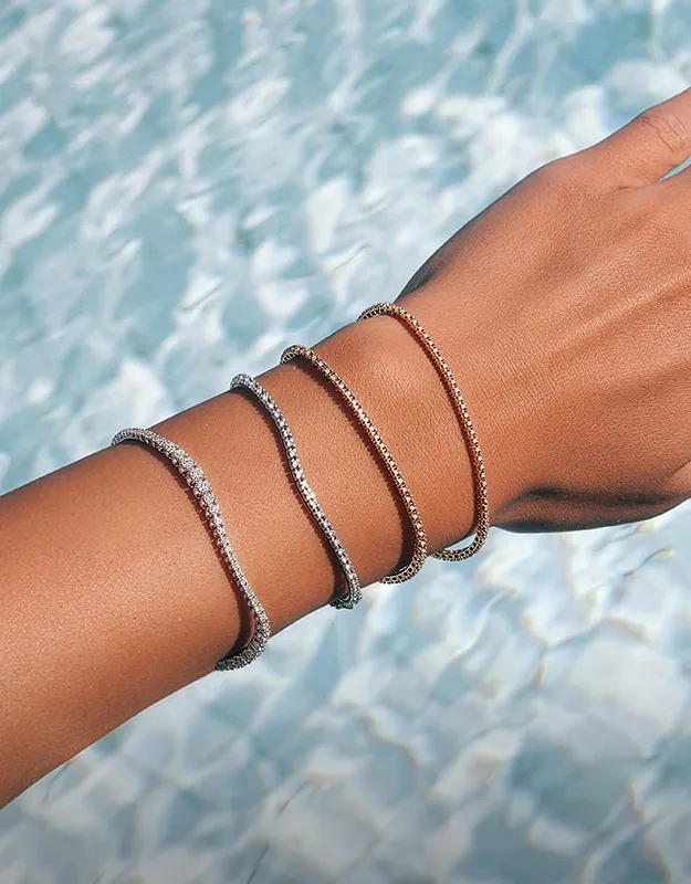 Elegant gold and silver bracelets stacked on a wrist against a water background.