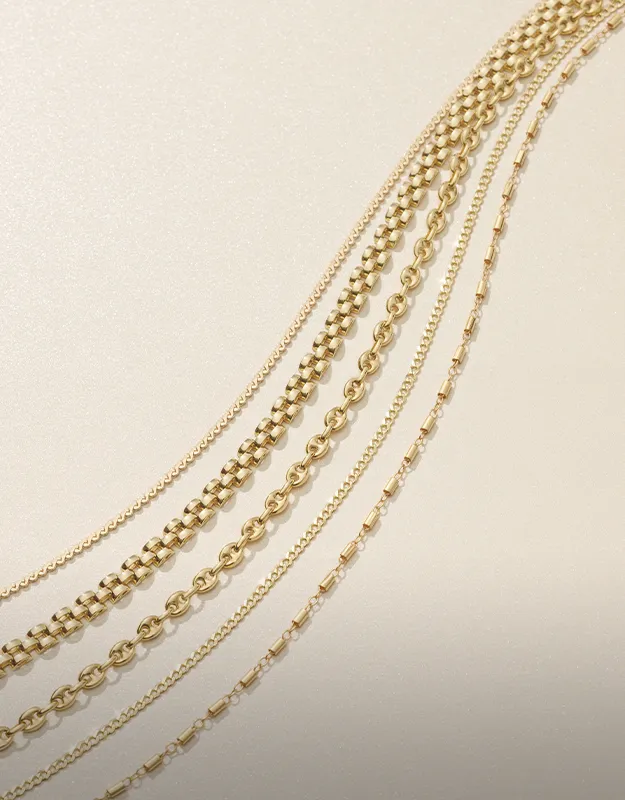 Layered gold chains with various link styles on a light background.
