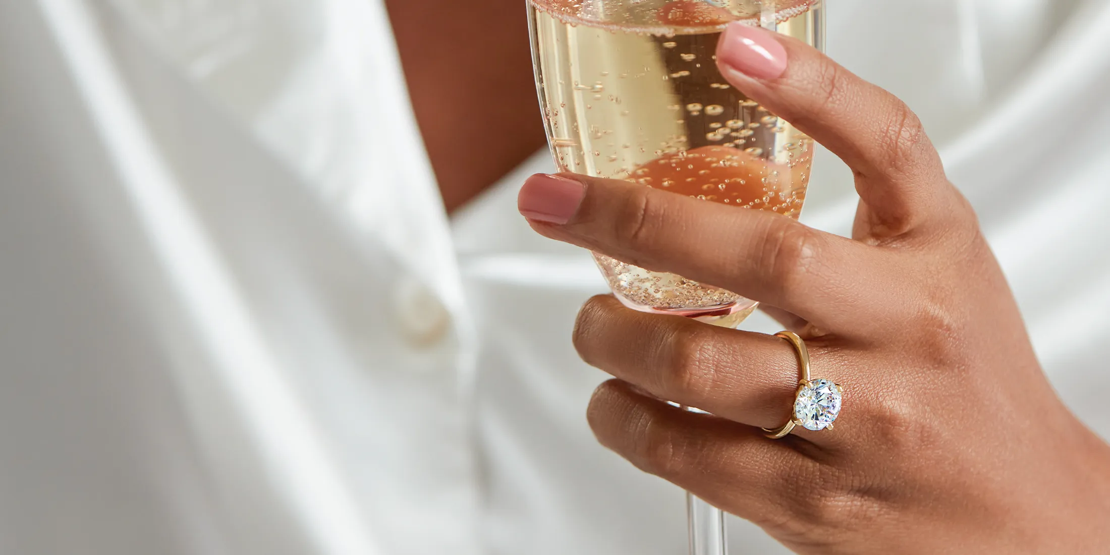 A hand with a diamond ring holds a glass of champagne.