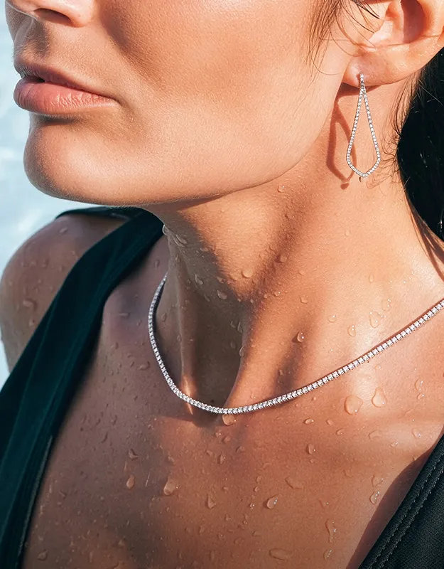 Model wearing diamond necklace and earrings with water droplets on skin.