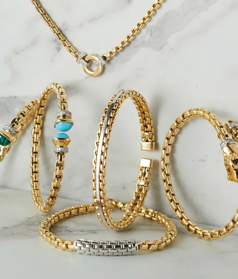 Gold chain bracelets and necklace with gemstone accents on a marble surface.