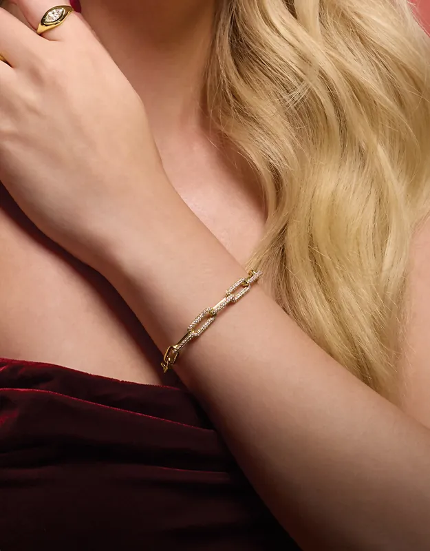 A woman wearing a gold bracelet and ring, with long blonde hair, in a burgundy dress.