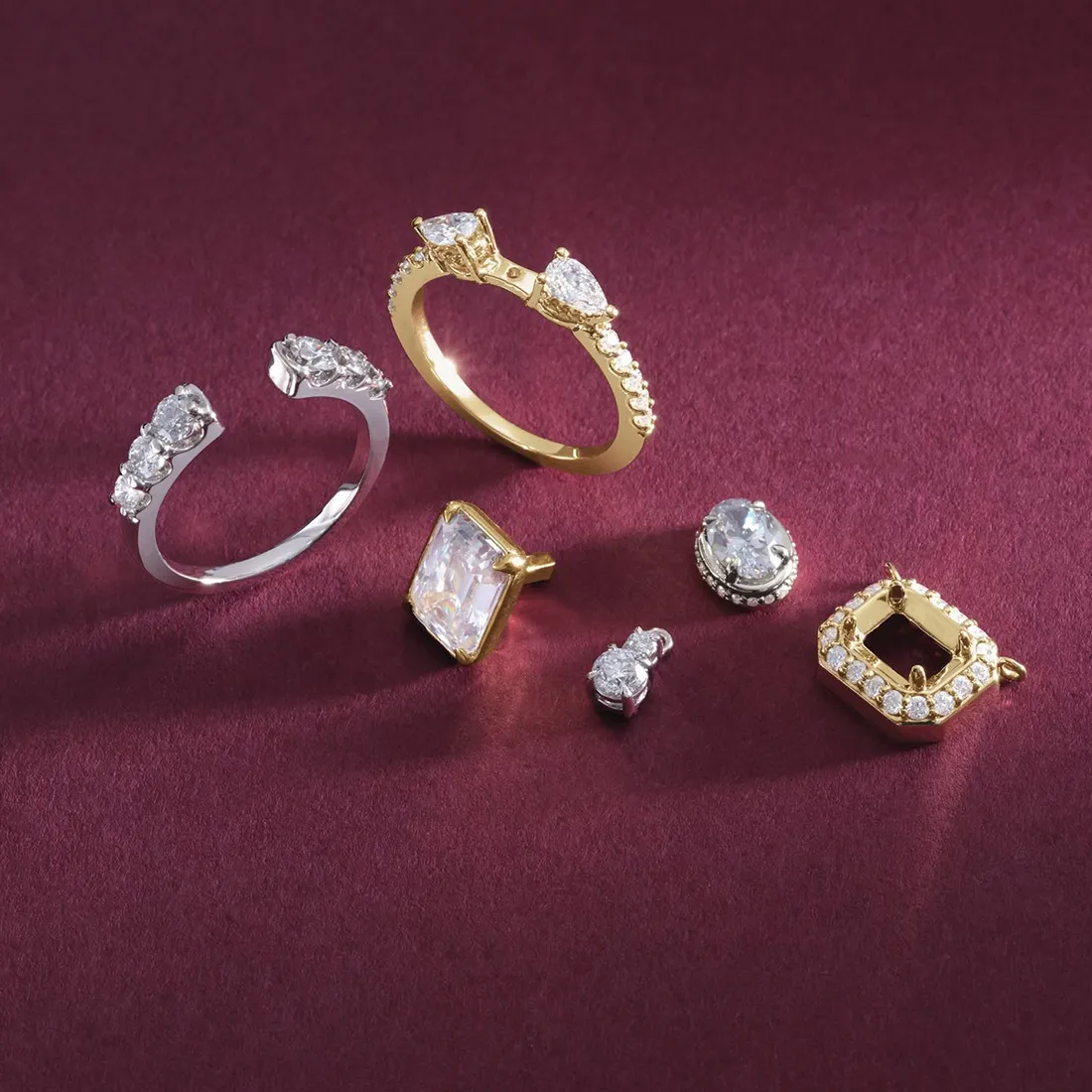 A collection of gold and silver rings and earrings with diamonds on a burgundy background.