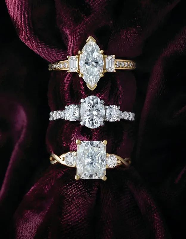 Three gold engagement rings with different diamond cuts on a dark velvet background.