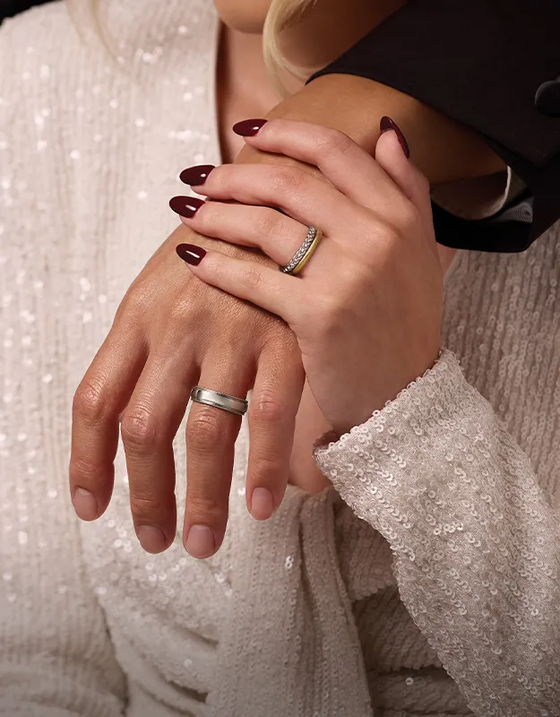 Two hands with wedding bands, one with red nails, in a close embrace.