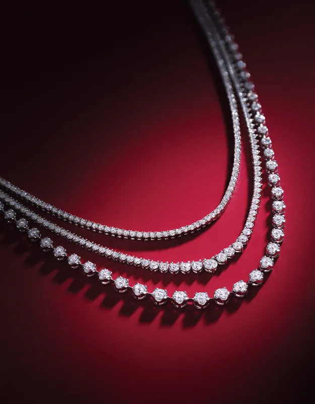 Three diamond necklaces elegantly displayed on a rich red background.
