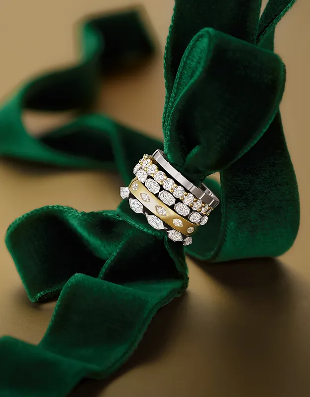 Three ornate rings with diamond accents on a green velvet ribbon.