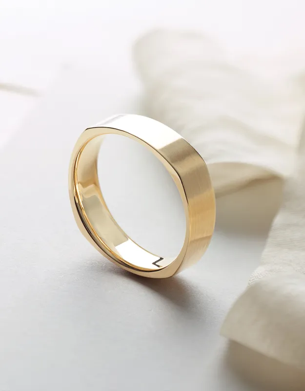 Men's gold wedding band displayed on a soft fabric background. Click to explore more at Futer Bros Jewelers.