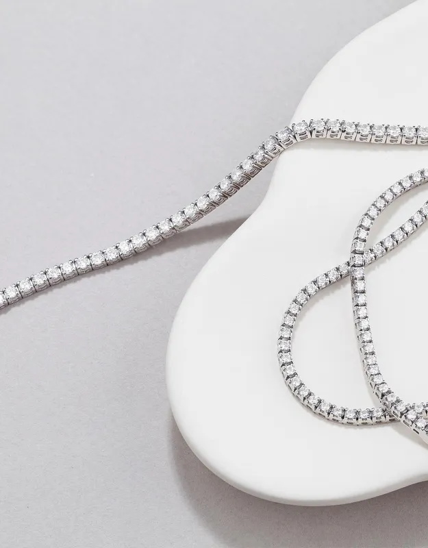 Elegant diamond necklaces displayed on a smooth white and gray surface.