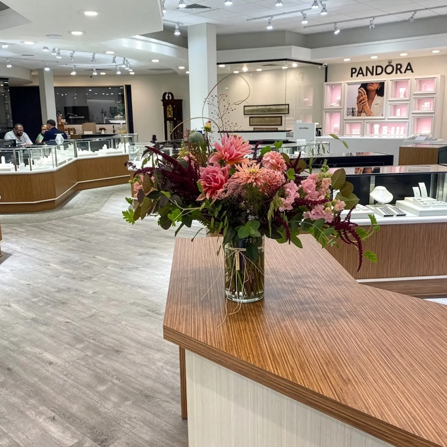 Floral arrangement on a wooden counter in a jewelry store with display cases and Pandora signage.