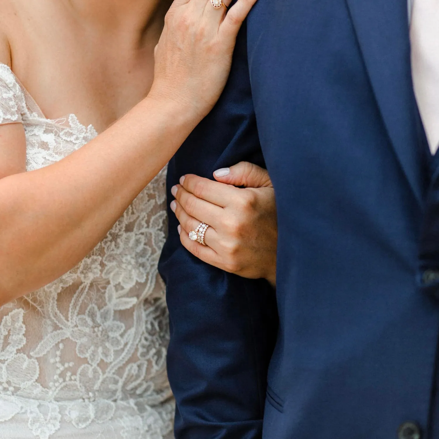 Close-up of a bride's hand with a diamond ring holding groom's arm in a blue suit.