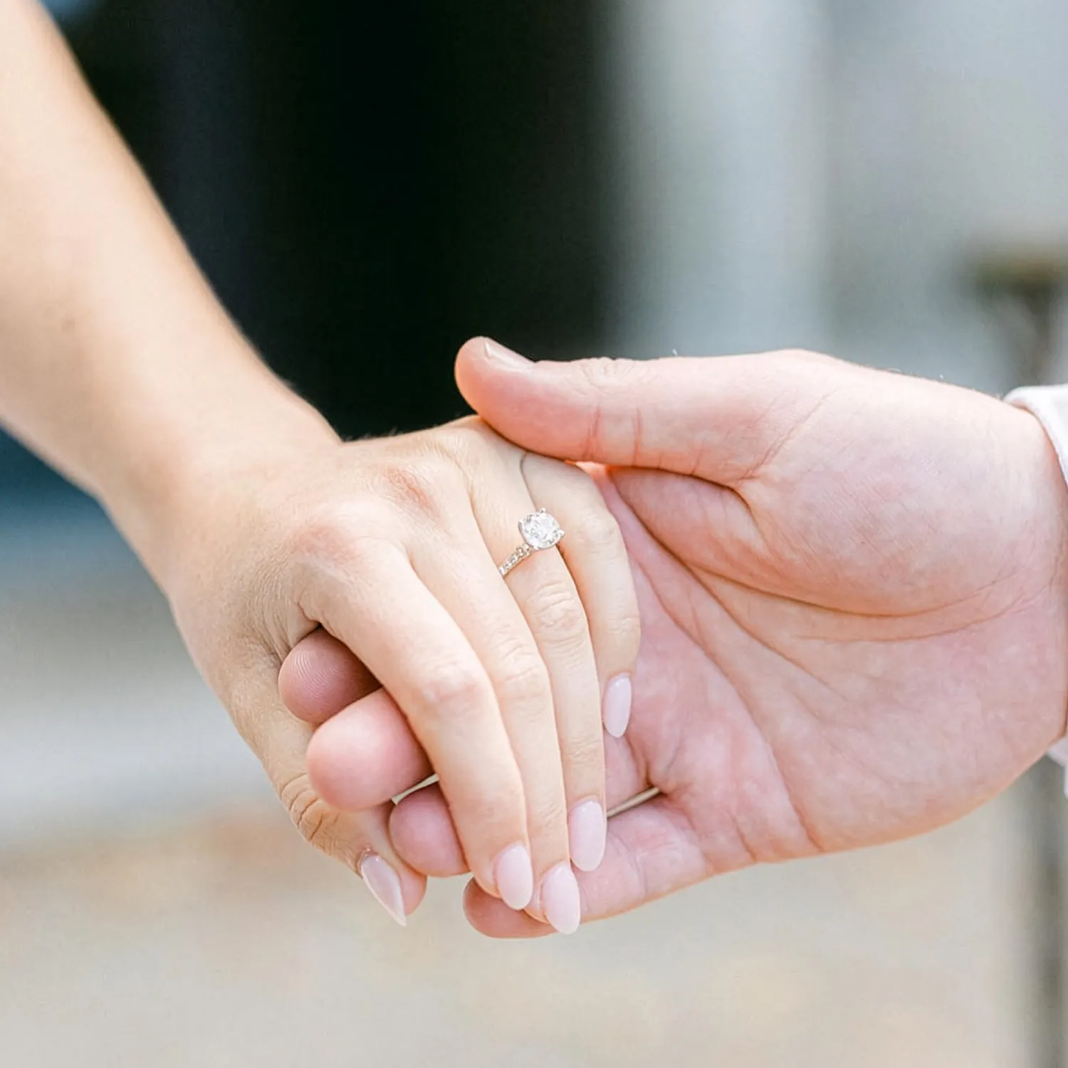 Two hands holding, one with an engagement ring.