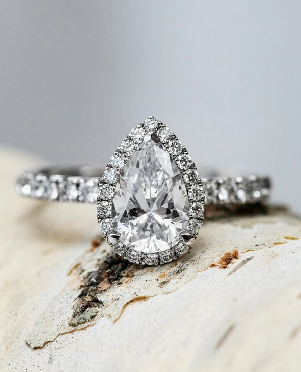 Pear-shaped diamond ring with halo setting on textured surface.
