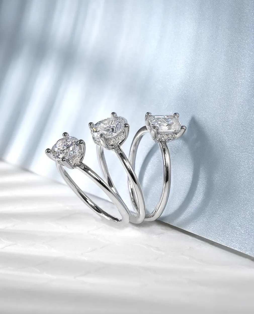 Three silver rings with large lab-grown diamonds on a light blue background.