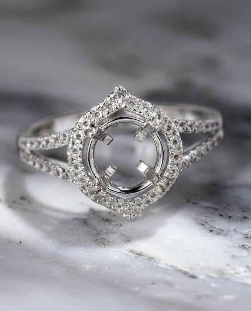 Elegant silver ring setting with intricate diamond detailing on a marble surface.